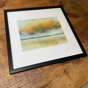 May include: A framed painting of a landscape with a yellow and orange sky reflected in a body of water. The painting is in a black frame.