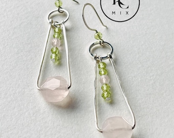 Könnte beinhalten: Silberne Ohrringe mit geometrischem Design und einem Anhänger aus rosa und grünen Edelsteinen. Die Ohrringe sind von LC Mix.