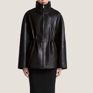 Könnte beinhalten: Eine schwarze Lederjacke mit hohem Stehkragen, durchgehendem Frontreißverschluss und langen Ärmeln. Die Jacke verfügt über eine geraffte Taille, die eine strukturierte Silhouette mit vertikalen Nahtlinien erzeugt.
