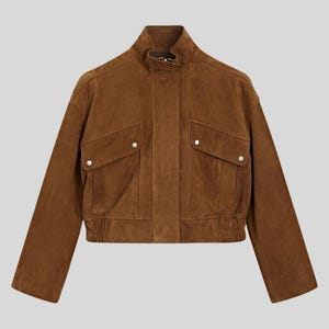 May include: A brown suede jacket with a stand-up collar and two front pockets. The jacket has a cropped fit with an elastic waistband and cuffs. The jacket is a solid color and has silver-colored button closures on the pockets.