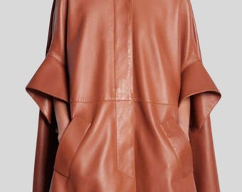 May include: A brown leather cape with a round neckline and a single decorative button closure. The cape features wide sleeves with flared cuffs and two front pockets. The garment is a solid color and has a tailored appearance.