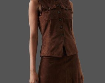 May include: A brown suede vest with two front pockets and a button-up closure. The vest is paired with a matching brown suede skirt. The outfit is a classic, timeless style.