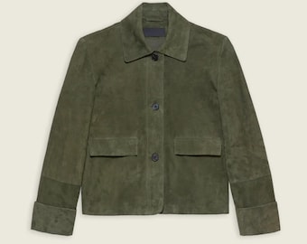 May include: Olive green suede jacket with a classic collar, two front pockets, and button closures. The jacket features long sleeves with folded cuffs. A stylish outerwear piece.