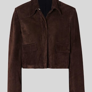 May include: A dark brown suede jacket featuring a collared neckline and two front pockets. The jacket has a cropped length and long sleeves. The color is a rich, dark brown.
