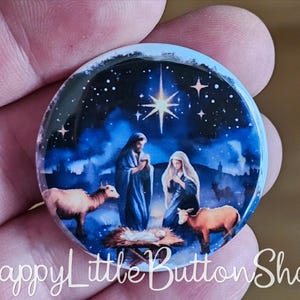 May include: A round button featuring a Nativity scene with Mary, Joseph, baby Jesus, and animals under a starry night sky. The button has a glossy finish and a blue and white color scheme. The text "Happy Little Button Shop" is at the bottom.