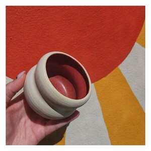May include: A small, white ceramic pot with a rounded, bulbous shape. The pot has a red interior and a textured exterior.