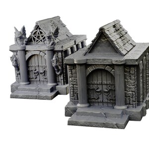 Op de afbeelding: Twee miniatuur stenen mausolea met gewelfde deuren en gedetailleerd steenwerk. Een mausoleum heeft waterspuwers en een pentagram op het dak.