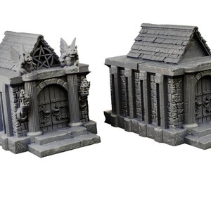 Op de afbeelding: Twee miniatuur grijze stenen mausoleums met gedetailleerde gravures en deuren. Een mausoleum heeft gargoyle-figuren en een pentagram-symbool op het dak.