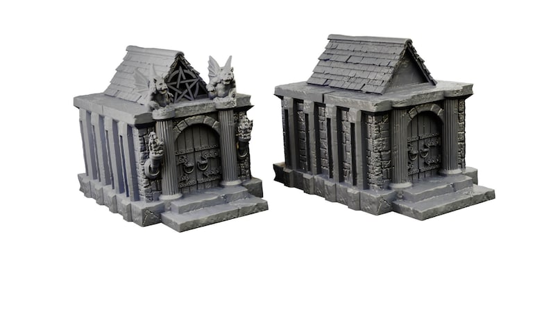 Op de afbeelding: Twee miniatuur grijze stenen mausoleums met gedetailleerde gravures en deuren. Een mausoleum heeft gargoyle-figuren en een pentagram-symbool op het dak.