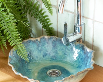 May include: A blue and white ceramic sink with a wavy edge. The sink has a drain in the center and is sitting on a wooden countertop. A chrome faucet is mounted to the wall behind the sink.