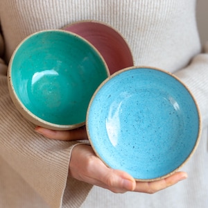 Può includere: Tre ciotole in ceramica di diversi colori: verde acqua, azzurro e rosa. Le ciotole sono punteggiate da macchie bianche e hanno una superficie leggermente ruvida.