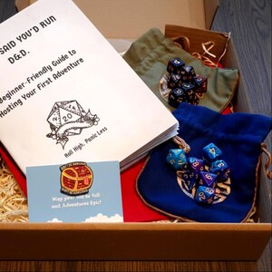 Puede incluir: Un kit de inicio de Dungeons & Dragons en una caja. Incluye una guía para principiantes, dados y pequeñas bolsas con cordón. La guía dice "SAID YOU'D RUN D&D. Beginner-Friendly Guide to Hosting Your First Adventure." Una tarjeta de visita dice "May your me be full and Adventures Epic!"
