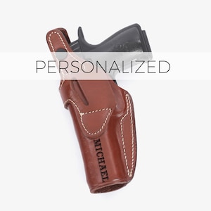 Puede incluir: Una funda de cuero marrón con una pistola negra en su interior. La funda está personalizada con el nombre "MICHAEL".