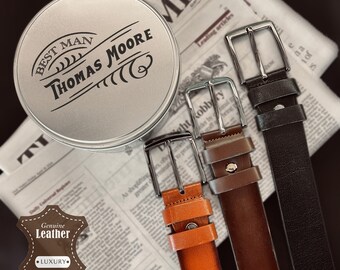 May include: A silver round tin with the text "Best Man Thomas Moore" on it. Three leather belts in brown, black, and orange are arranged on a newspaper background.