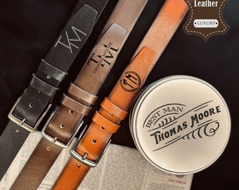 May include: Three leather belts with different engravings. The belts are brown, black, and orange. The belts are arranged on a newspaper with a round tin container that says "Best Man Thomas Moore". The tin container has a label that says "Genuine Leather Luxury".