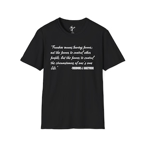 May include: Black t-shirt with white text. The text reads: "Freedom means having power; not the power to control other people, but the power to control the circumstances of one's own life." -THEODORE J. KACZYNSKI. The shirt has a crew neck and short sleeves.