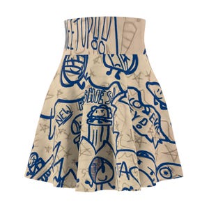 May include: A beige skater skirt with a high waist, covered in blue and gray graffiti-style drawings and text. The skirt features various doodles, including faces, stars, and the word "NEW".