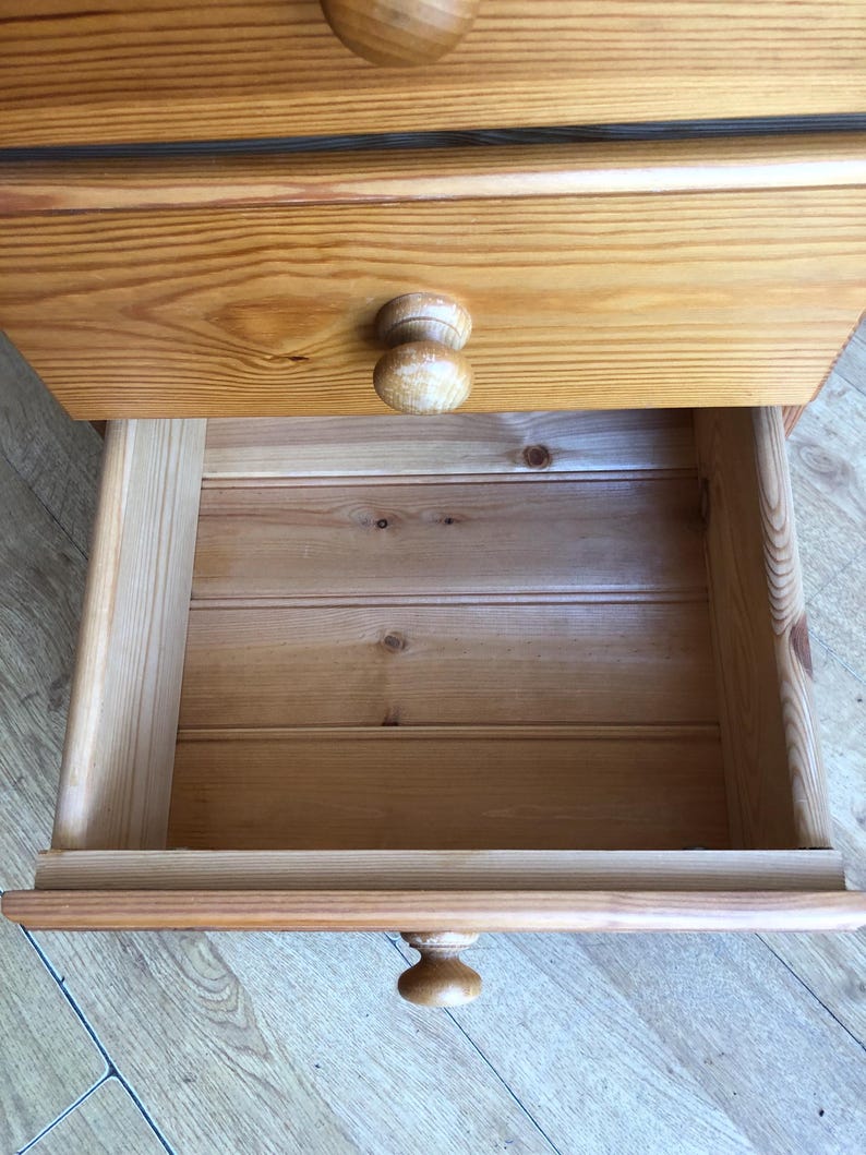 K&ouml;nnte beinhalten: Eine hellbraune Holzkommode mit nat&uuml;rlicher Holzmaserung. Das M&ouml;belst&uuml;ck verf&uuml;gt &uuml;ber mehrere horizontale Schubladen, die jeweils mit einem runden Holzknauf ausgestattet sind. Eine Schublade ist ge&ouml;ffnet und zeigt das Innere.
