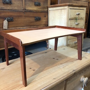 May include: A small wooden table with a light brown top and dark brown legs. The table is sitting on a wooden surface.