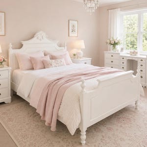 May include: A white wooden bed frame with a white headboard and footboard, dressed in white bedding and a soft pink throw blanket. The bed is flanked by two white three-drawer nightstands with lamps, and a matching white vanity with drawers.