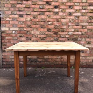 May include: A rectangular wooden table with a light-coloured top and four brown legs. The table's top has a natural, unfinished edge. The table is approximately 91 cm long and 76 cm wide.