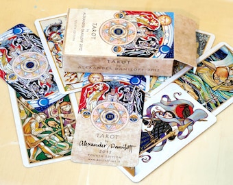May include: A set of tarot cards with colorful illustrations and gold accents. The cards feature a variety of characters and symbols, including a knight, a queen, and a king. The cards are arranged in a fan shape, with the top card showing a knight on horseback. The text on the cards reads "Tarot by Alexander Daniloff 2012 Fourth Edition".