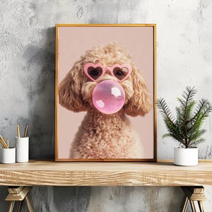 May include: A light brown poodle wearing pink heart-shaped sunglasses and blowing a pink bubble. The dog is looking directly at the camera.