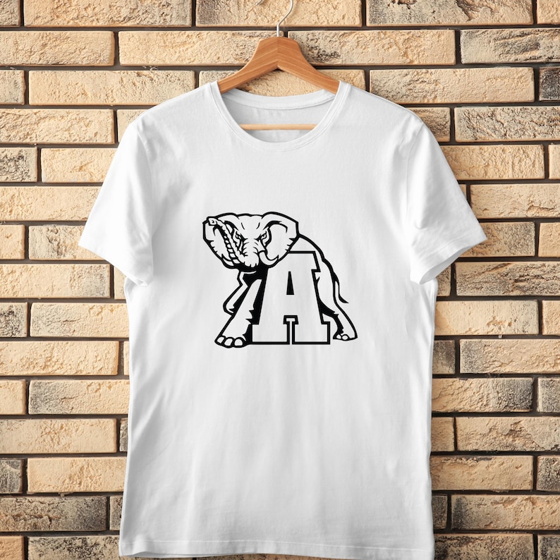 Pu&ograve; includere: T-shirt bianco con grafica nera di un elefante e la lettera 'A'. Il disegno &egrave; centrato sulla maglietta, appesa a una gruccia di legno. Lo sfondo &egrave; un muro di mattoni. La grafica &egrave; un design audace e semplice.