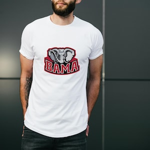 Pu&ograve; includere: T-shirt bianca con grafica di una testa di elefante e la scritta "BAMA" in rosso e bianco. La maglietta &egrave; realizzata in materiale morbido, adatta per un abbigliamento casual. Il design &egrave; un logo di una squadra sportiva.