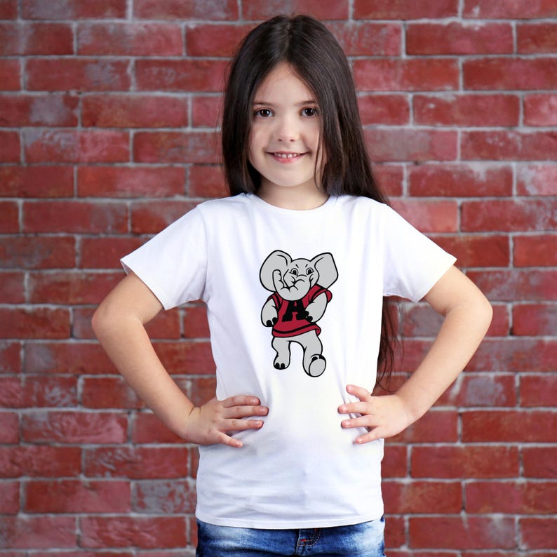 Pu&ograve; includere: Una maglietta bianca con un elefante dei cartoni animati che indossa una maglia rossa con una "A" nera. L'elefante ha le orecchie grigie ed &egrave; in piedi con le braccia lungo i fianchi. La maglietta &egrave; indossata da una persona giovane.