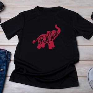 Pu&ograve; includere: T-shirt nero con un disegno di elefante rosso e la scritta "Roll Tide". La grafica &egrave; in un font script. La maglietta &egrave; realizzata in un materiale morbido, adatto per un abbigliamento casual. Il design &egrave; centrato sul davanti.