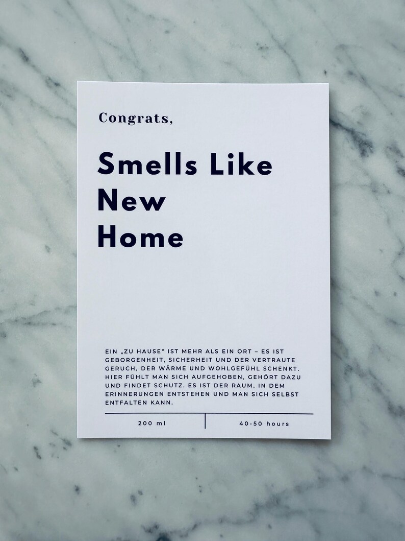 May include: White card with black text that reads "Congrats, Smells Like New Home". The card also includes the text "Ein zu Hause' ist mehr als ein Ort - es ist Geborgenheint, Sicherheit und der vertraute Geruch, der W&auml;rme und Wohlgef&uuml;hl schenkt. Hier f&uuml;hlt man sich aufgehoben, geh&ouml;rt dazu und findet Schutz. Es ist der Raum, in dem Erinnerungen entstehen und man sich selbst entfalten kann."  The card also includes the text "200 ml" and "40-50 hours".