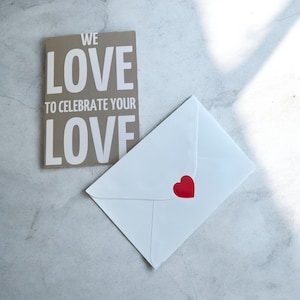 May include: A brown card with the text "We love to celebrate your love" and a white envelope with a red heart sticker.