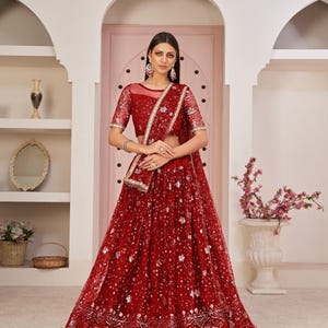 May include: A red net lehenga with silver embroidery and sequins. The lehenga has a matching dupatta and a red blouse with a net overlay.
