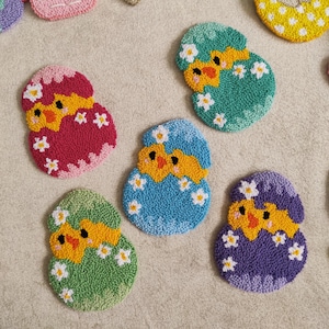 May include: Handmade Easter egg-shaped coasters in various colors, including pink, green, blue, and purple. Each coaster features a yellow chick design with white flower accents, perfect for spring decor.