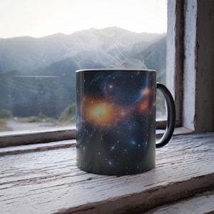 Puede incluir: Una taza de café negra con un diseño de impresión de galaxia. El vapor se eleva de la taza, que está sentada sobre una superficie de madera blanca cerca de una ventana.