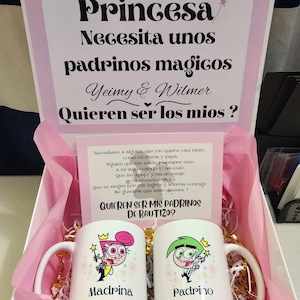 May include: A pink gift box with a white card that says "Toda Princesa Necesita unos padrinos magicos Yeimy & Wilmer Quieren ser los mios?" and a smaller card that says "Necesitare a alguien que me quiera casi tanto como mi mama y papa. Alguien que me cuide y siempre este a mi lado cuando to necesite, Que me apoyo y me aconseje en los momentos dificiles. Que se alegre por mis logros y sonria conmigo. Me gustaria que sean ustedes! Quieren ser mis padrinos de bautizo?" The box contains two white mugs with cartoon characters and the words "Madrina" and "Padrino" on them.