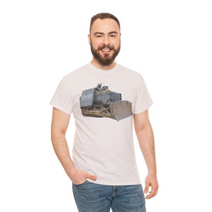 Może przedstawiać: Jasnoróżowa koszulka z szczegółową ilustracją spychacza. Spychacz jest głównie szary z brązowymi i żółtymi akcentami. Koszulka ma klasyczny okrągły dekolt.