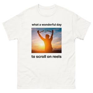 May include: A white t-shirt with a silhouette of a person breaking free from chains against a sunset background. The text "what a wonderful day to scroll on reels" is printed on the shirt.