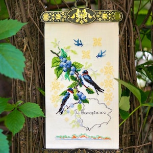 May include: A cross-stitched wall hanging featuring three swallows perched on a branch with blue berries. The artwork includes the word "Запоріжжя" and is framed by decorative metal bars with floral designs.