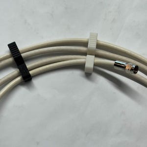 May include: A close-up of several off-white coaxial cables secured with black and white cable clips. The cables have a silver connector on the end. The background is a plain white surface.