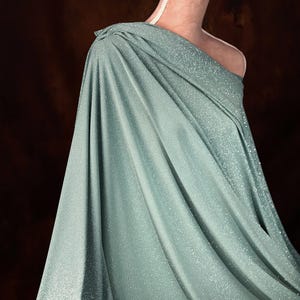 A close-up of a woman wearing a shimmering green dress with a draped, flowing silhouette.