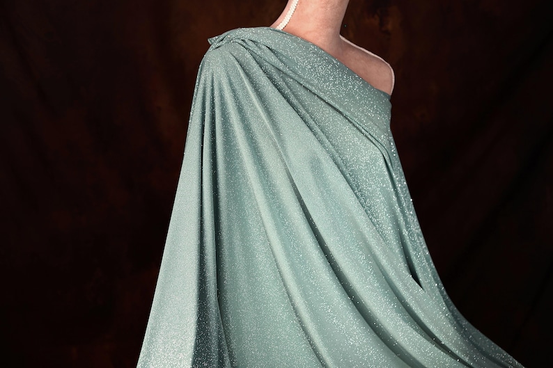 A close-up of a woman wearing a shimmering green dress with a draped, flowing silhouette.