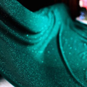 A close-up view of a shiny, turquoise-colored fabric with a sparkling texture, creating a visually striking and vibrant image.
