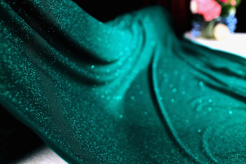 A close-up view of a shiny, turquoise-colored fabric with a sparkling texture, creating a visually striking and vibrant image.