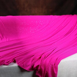 A close-up image of a vibrant pink fabric with sparkles, draped over a white surface.