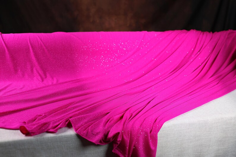 A close-up image of a vibrant pink fabric with sparkles, draped over a white surface.