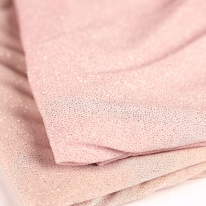 A close-up image of a fabric with a pink or peach-colored texture, featuring small, glittery dots or specks that create a sparkling effect.