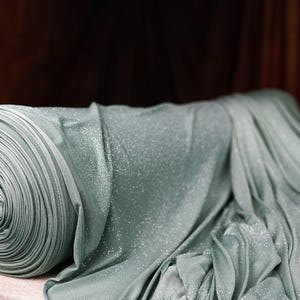 A close-up view of a roll of shimmering blue fabric with a floral pattern, placed on a table against a dark background.