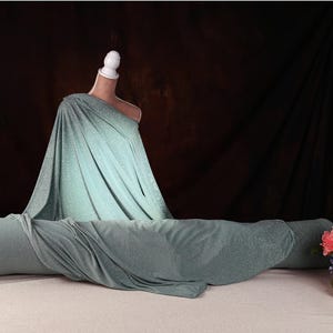 a mannequin wearing a green dress, with a vase of flowers placed next to it on a table.